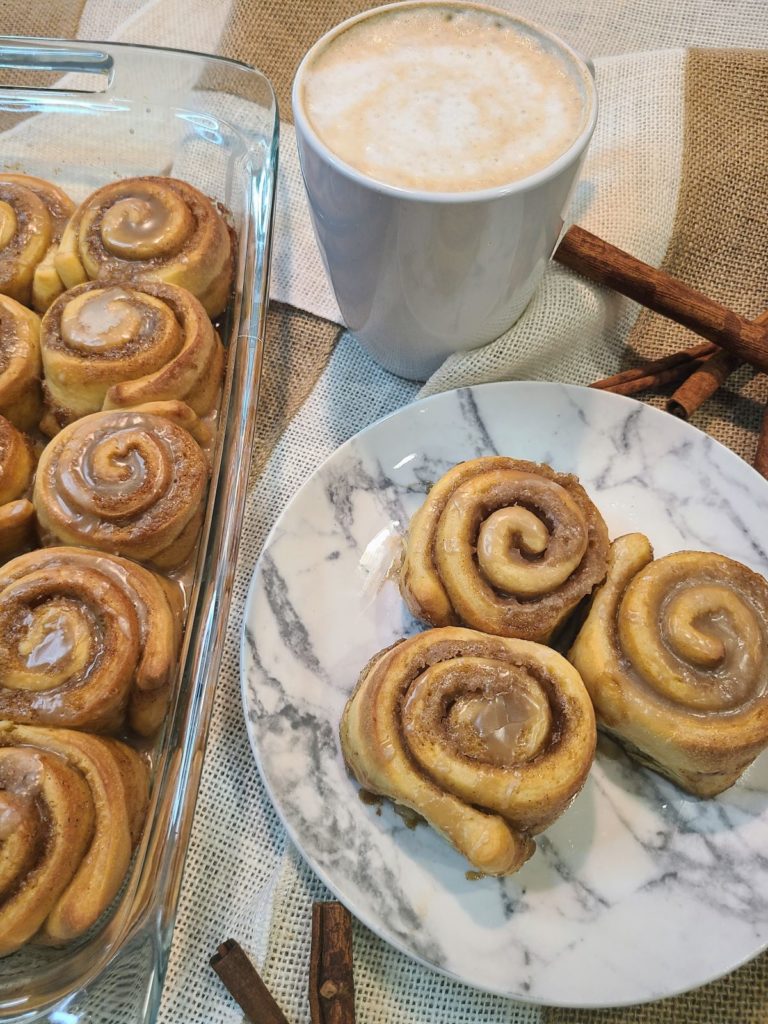 A plate of 3 cinnamon maple rolls with a cup of coffee