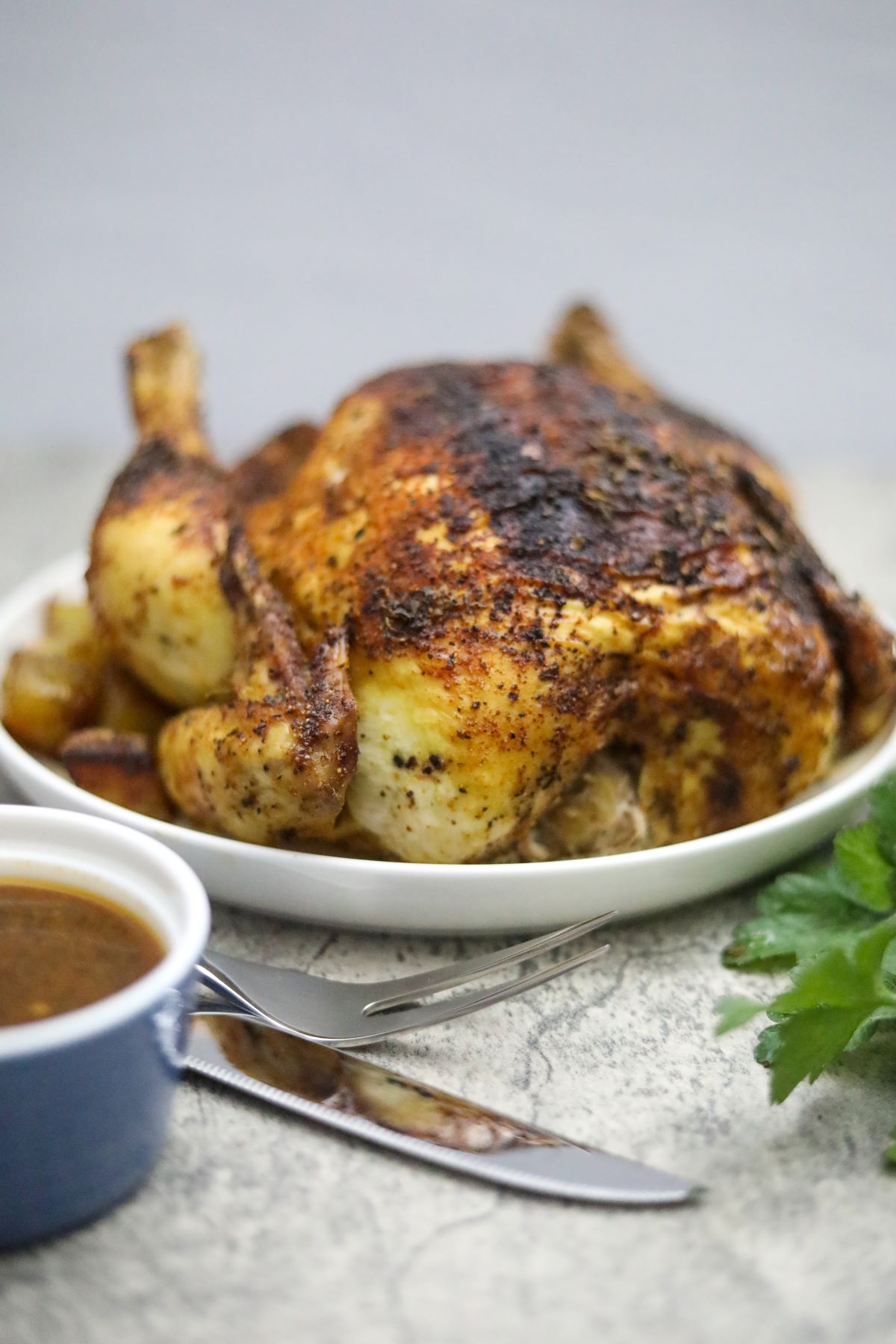 Vertical image of a roasted blackened chicken on a plate with carving knfe