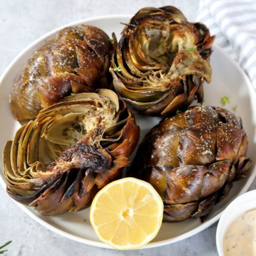 Roasted artichokes on a white plate with a lemon
