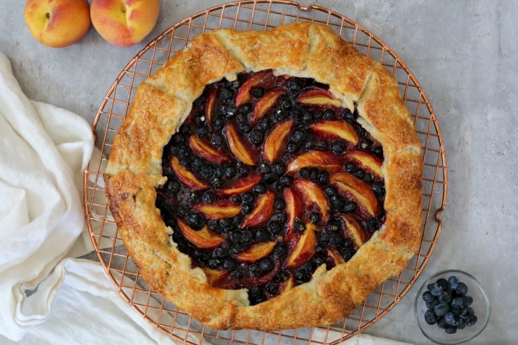 blueberry peach galette on a cooling rack with a small bowl of blueberries