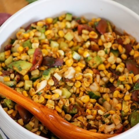 Corn salad in a white bowl with a wooden spoon