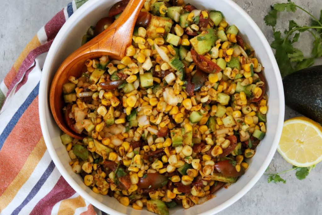 a bowl of corn salad with a wooden spoon in it