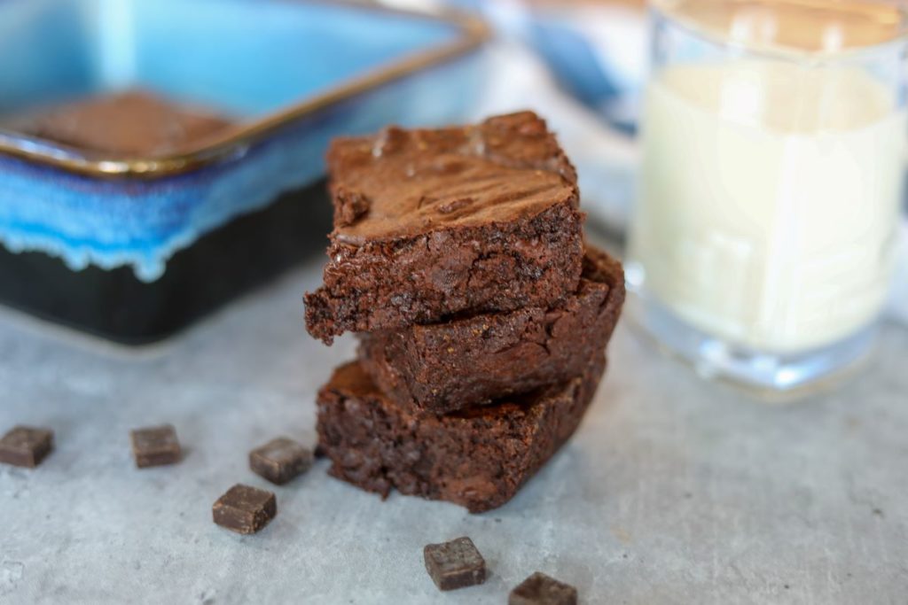 A stack of three brownies with a glass of milk