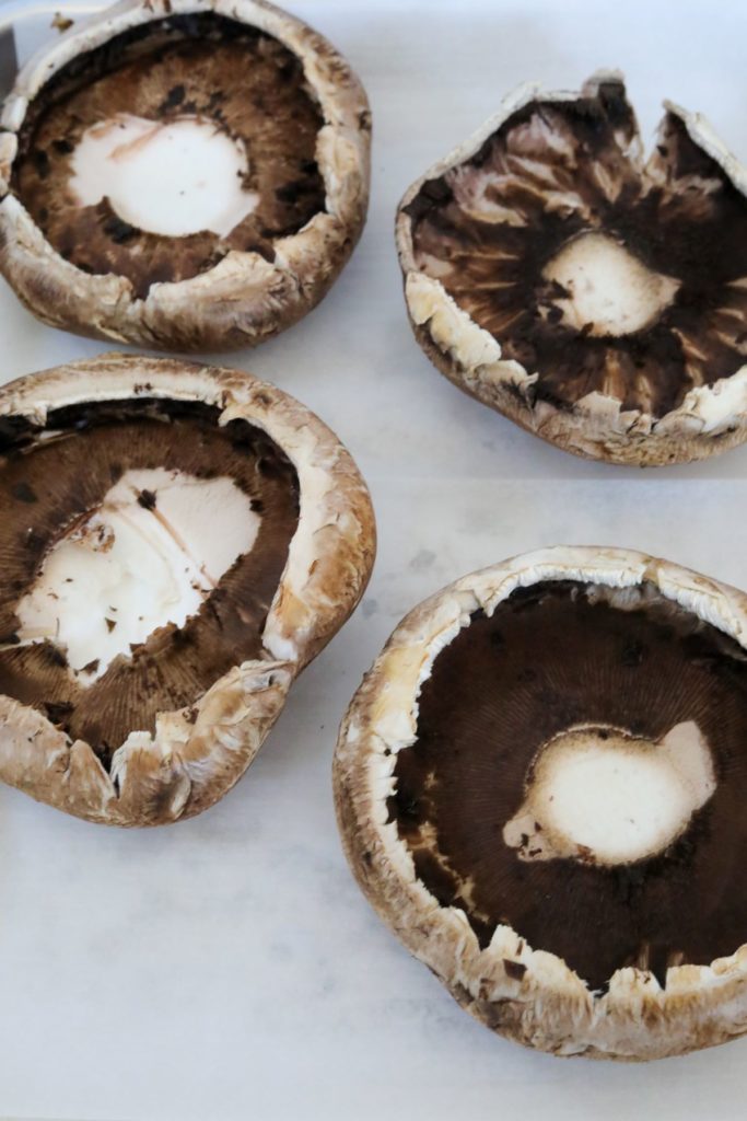 Four portobello mushrooms one a lined sheet pan with gills removed