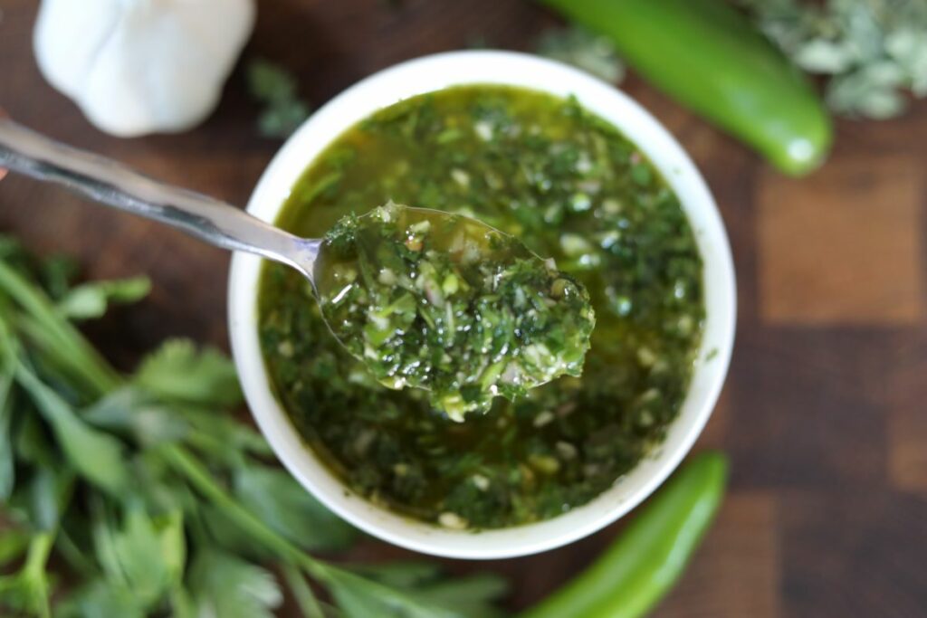 close up of a spoon of chimichurri sauce over a bowl of the rest of the sauce
