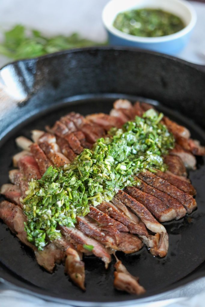 cast iron skillet with sliced pan seared steak topped with chimichurri sauce