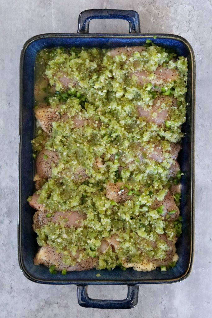 Chicken in a baking dish covered in salsa verde, jalapenos, and cilantro.