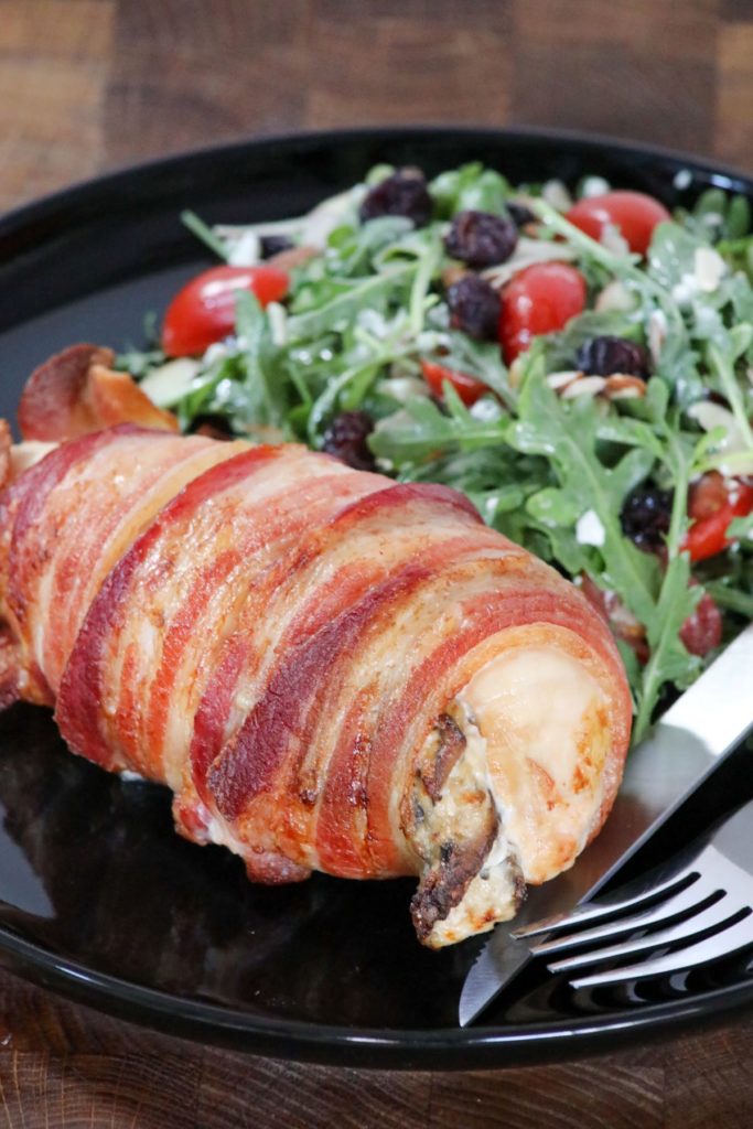 Bacon wrapped stuffed chicken breast on a black plate with salad