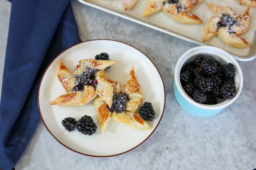 blackberry pinwheels on a white plate in front of a sheet pan with more pinwheels