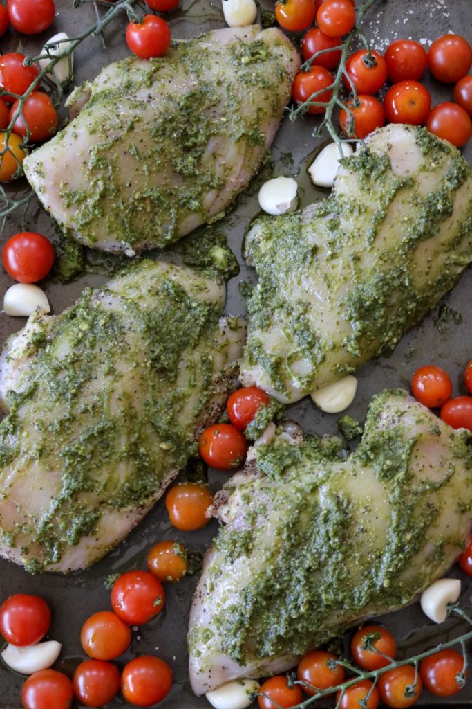 Uncooked chicken covered in pesto with tomatoes and garlic