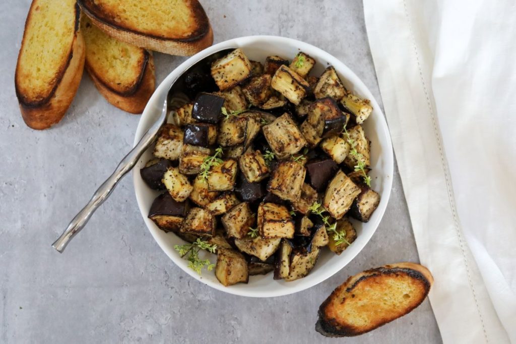 Roasted eggplant in a white bowl with toasted bread