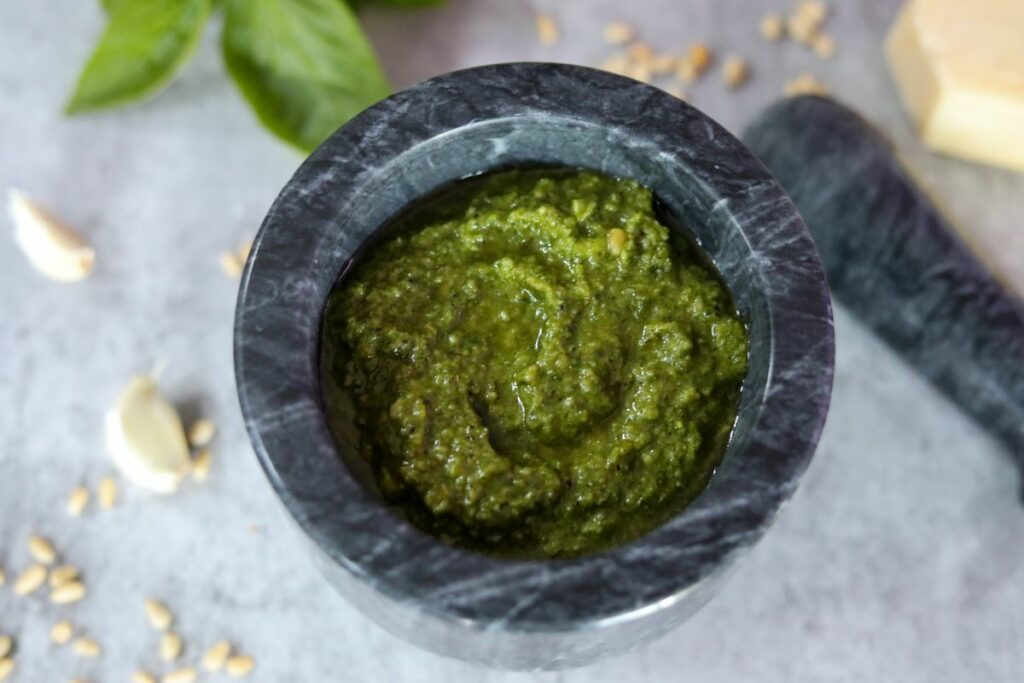 mortar full of basil pesto with pestle on the side