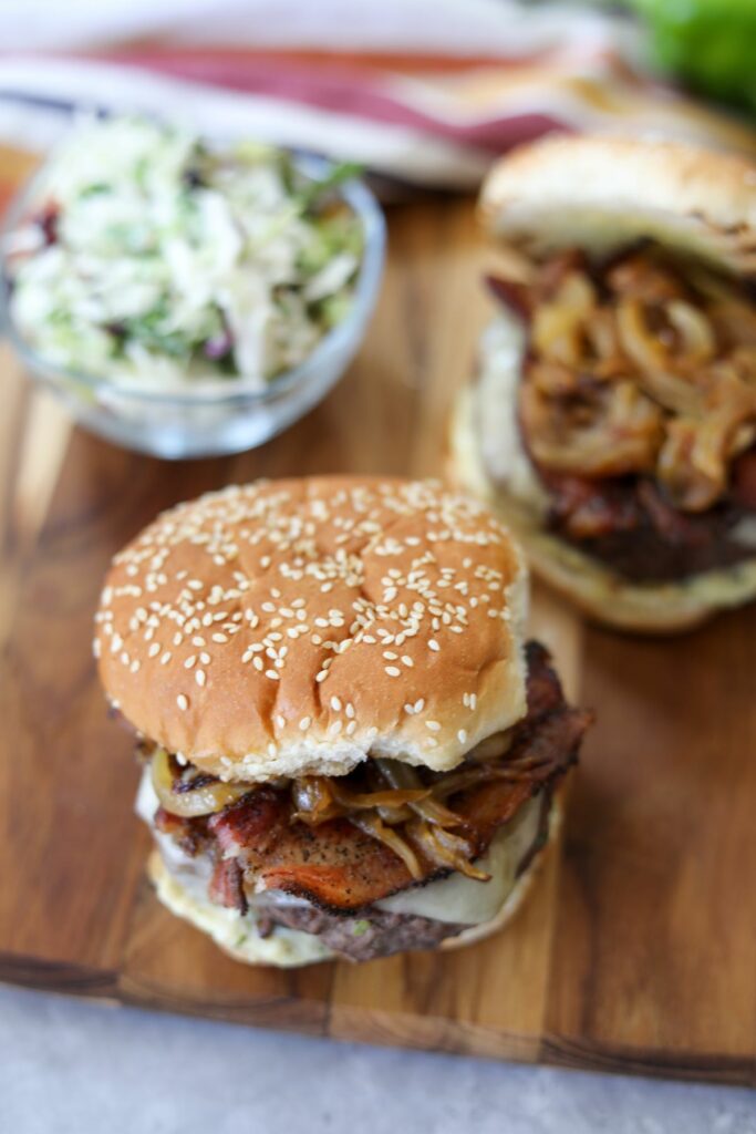 Two hamburgers on a wooden serving board with a bowl of coleslaw