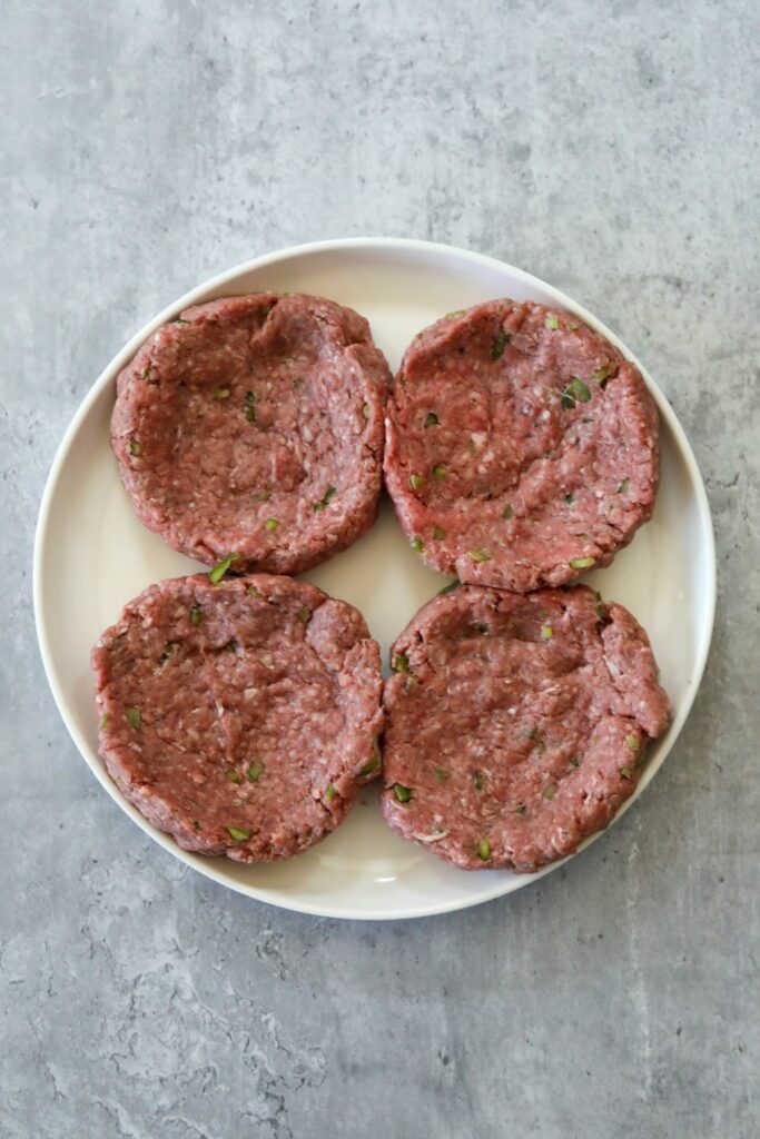 Uncooked beef patties on a white plate.