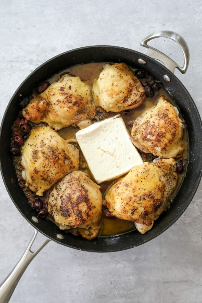 Cooked chicken in a pan with a block of feta cheese