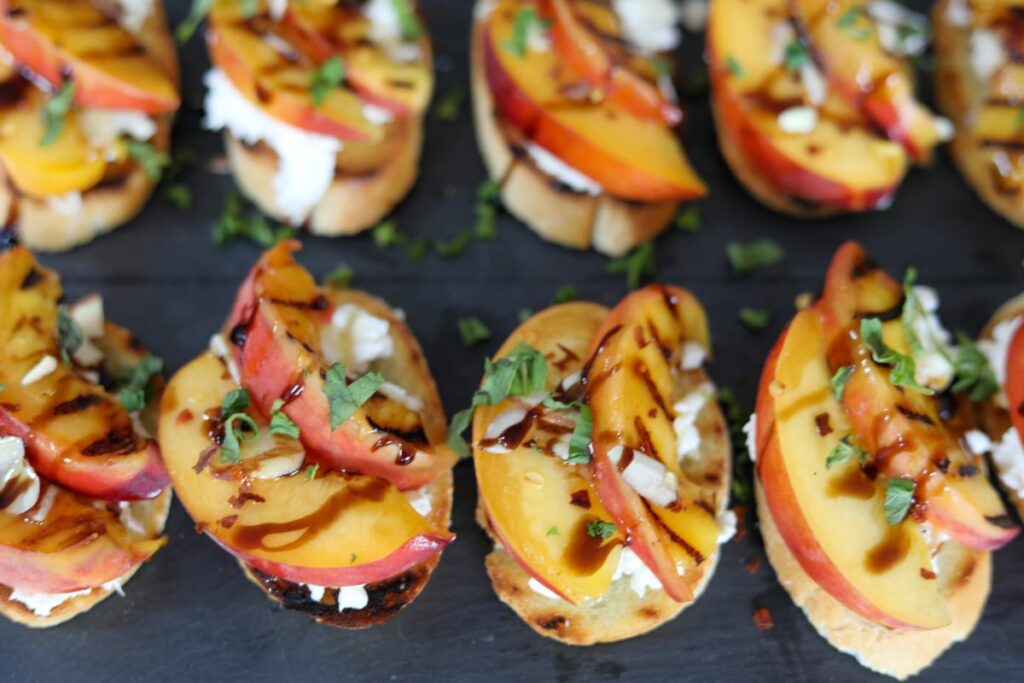 Grilled peach crostini topped with mint on a slate plate.