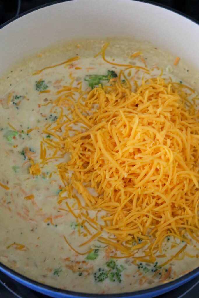 Shredded cheddar cheese added to soup in a Dutch oven