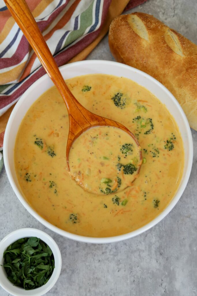 A ladel full of broccoli and cheddar soup in a white bowl