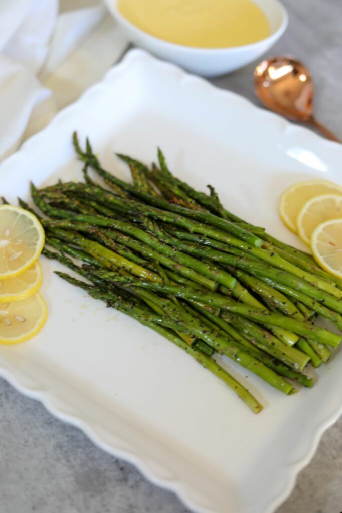 Roasted asparagus on a white platter with a bowl of hollandaise