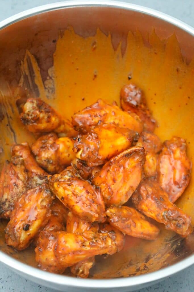 Wings tossed in buffalo sauce in a metal mixing bowl