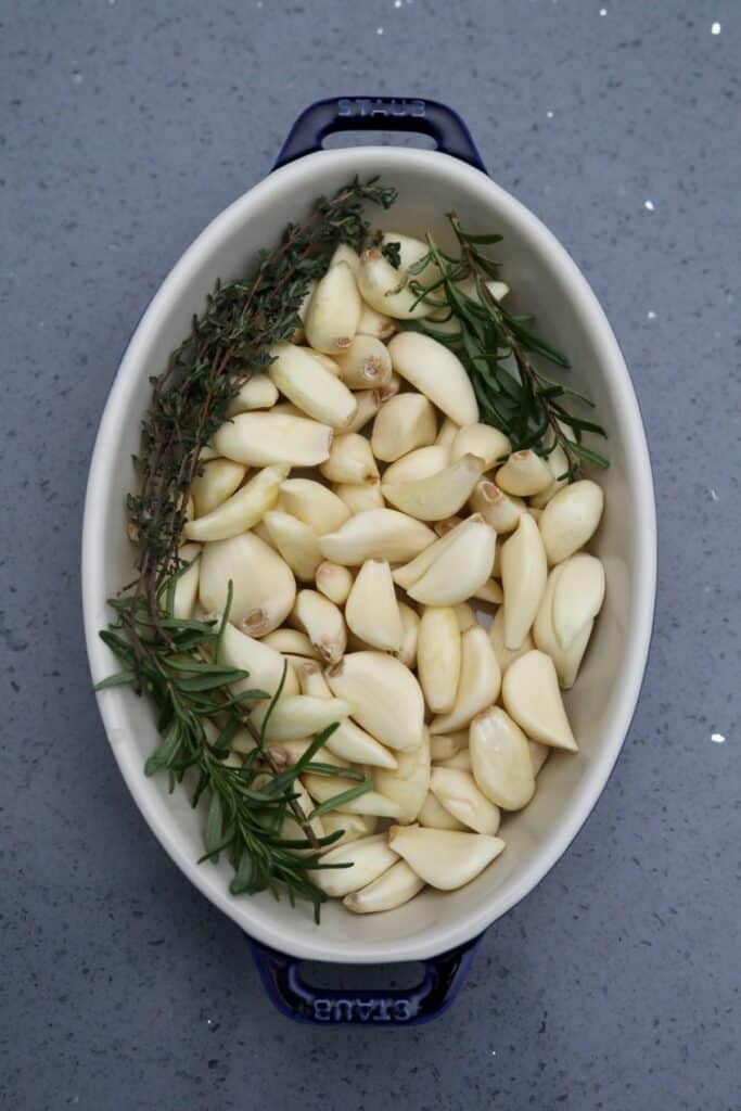 Peeled garlic cloves and herbs in a baking dish
