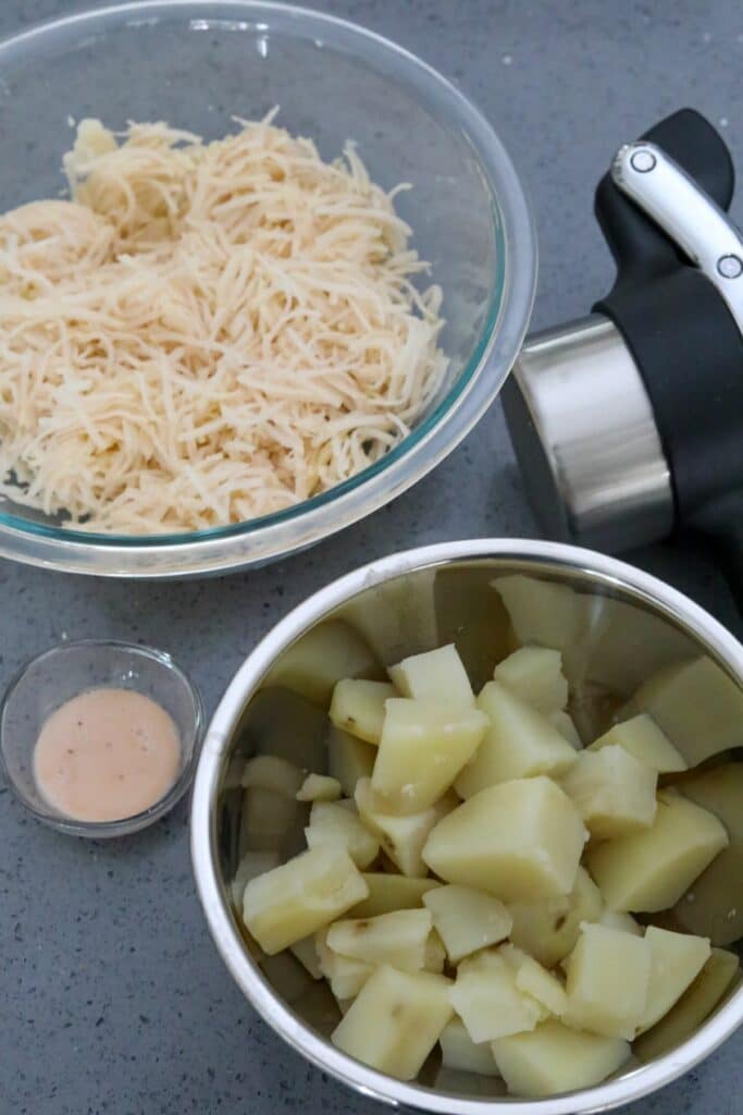 Boiled and grated potatoes in two bowls with a potato ricer.