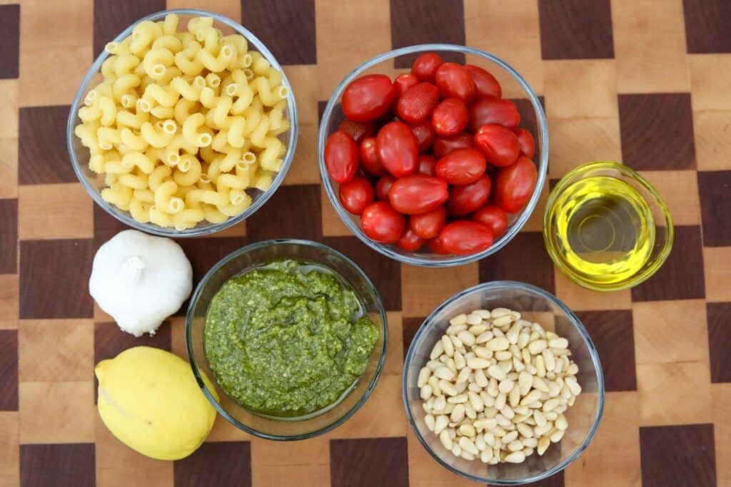 Ingredients for pesto pasta on a wooden cutting board