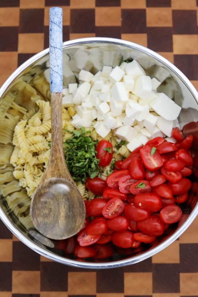 A mixing bowl with pasta salad ingredients
