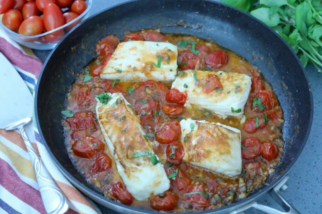 A pan with seared halibut on top of tomato suace