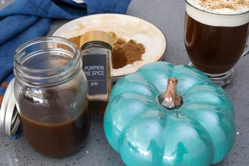 A jar of pumpkin spice syrup next to a blue pumpkin