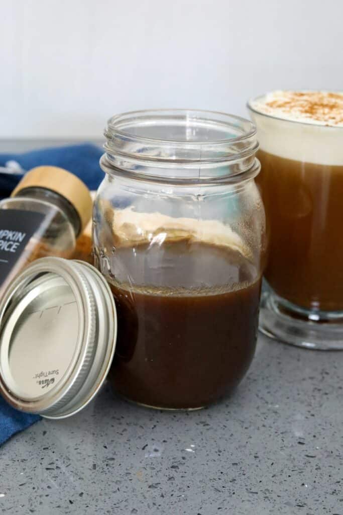 A jar of pumpkin spice syrup with a cup a coffee