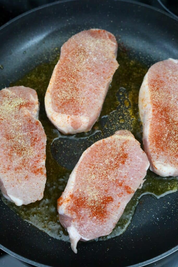 Four seasoned pork chops on a pan with oil