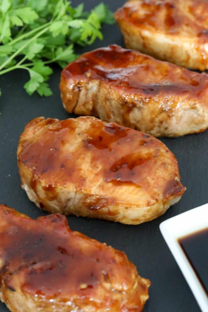 Vertical photo of 4 glazed pork chops on a slate plate