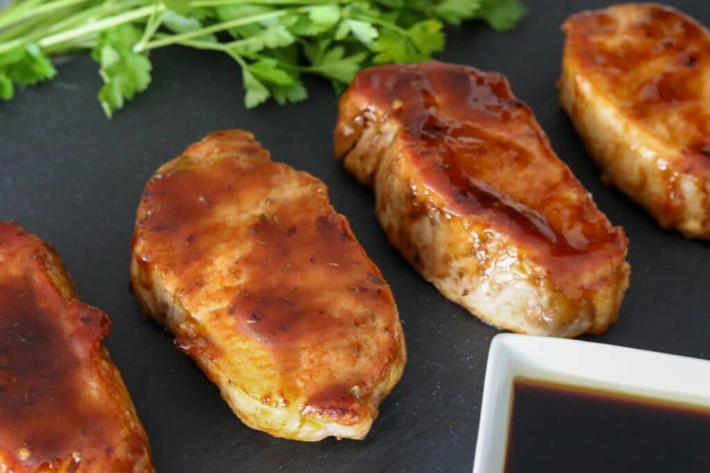 Horizontal photo of 4 glazed pork chops on a slate plate with parsley