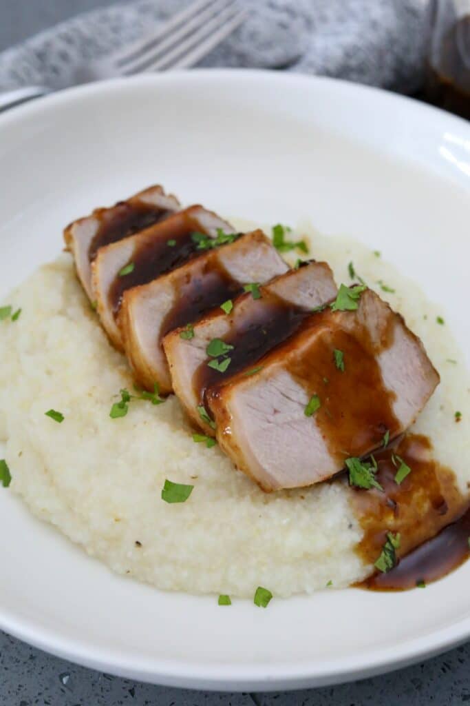 Sliced glazed pork chop on a bed of grits in a white bowl
