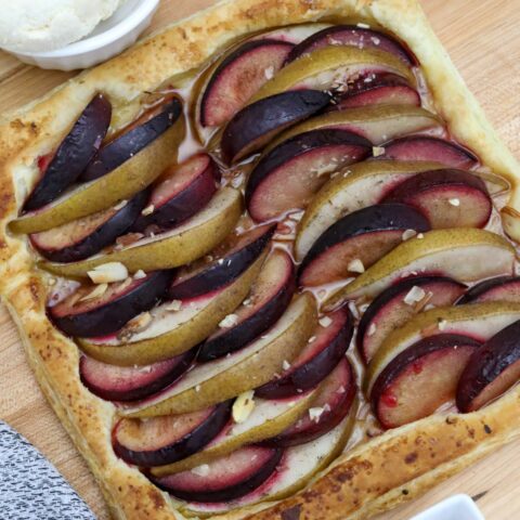 A pear and plum tart on a wooden cutting board