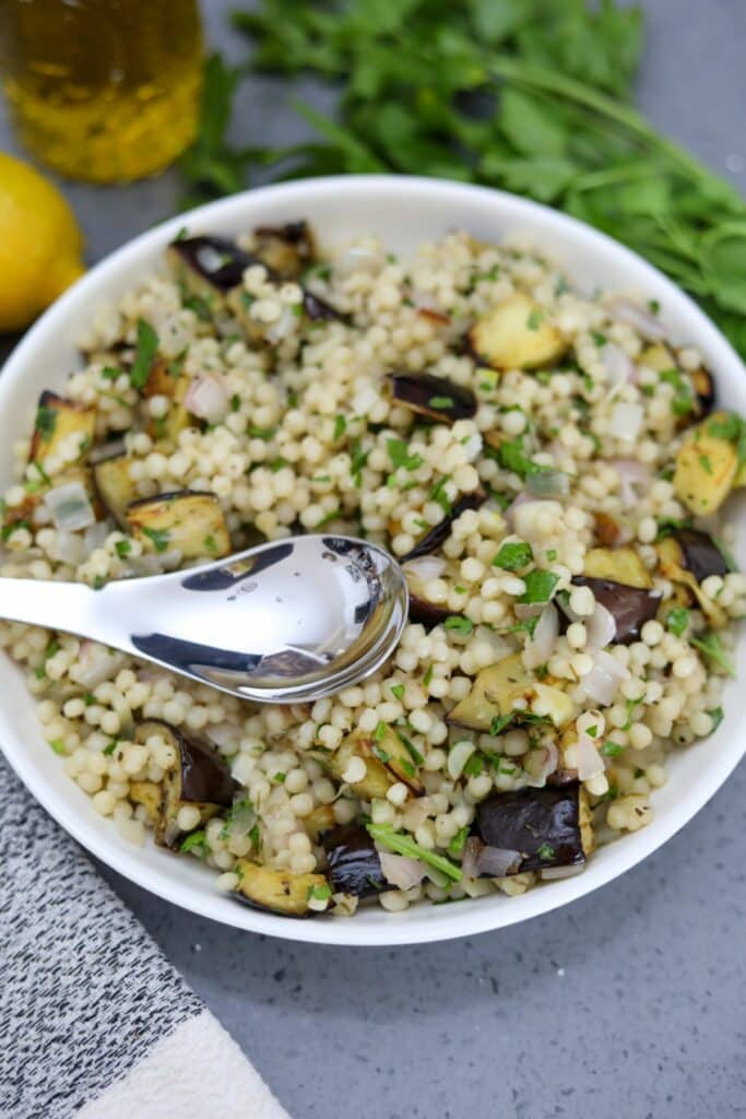 A spoon in a bowl of roasted eggplant Israeli couscous