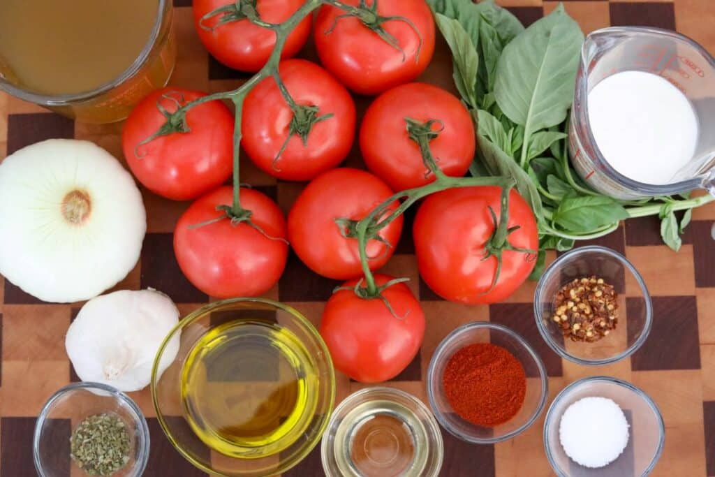 Ingredients for roasted tomato soup on a wooden cutting board