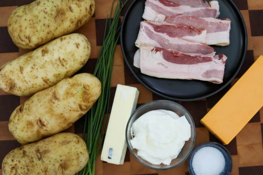 Ingredients for twice baked potato on a wooden cutting board