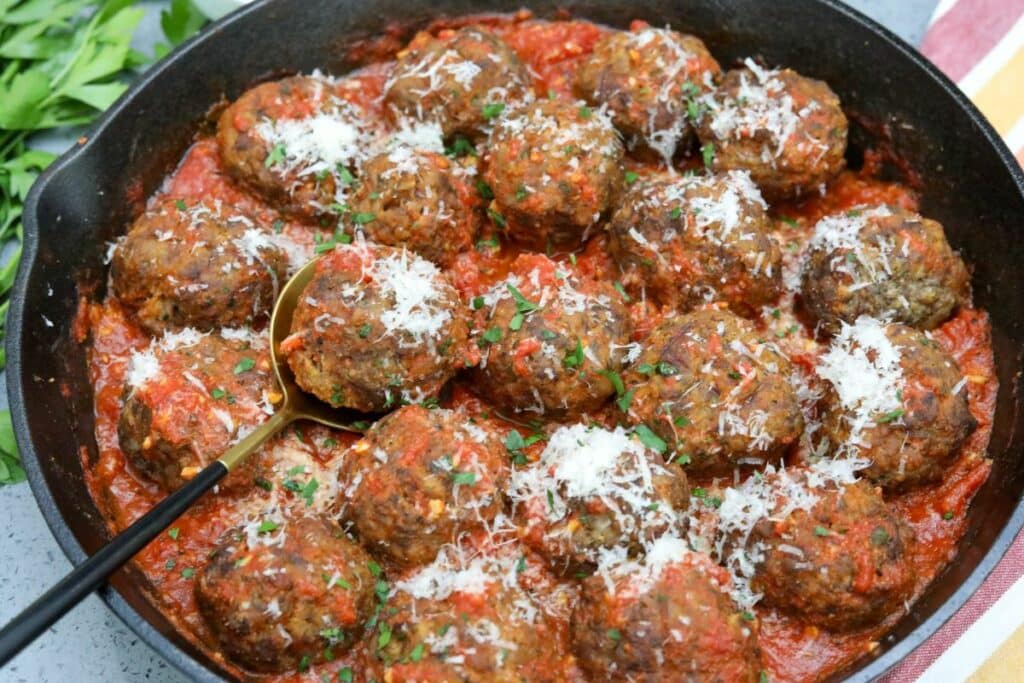 Cast iron skillet filled with Italian meatballs and tomato sauce with a serving spoon under a single meatball