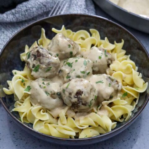 A blue bowl with egg noodles topped with Swedish meatballs