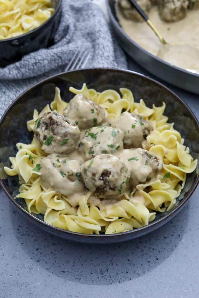 A blue bowl with egg noodles topped with Swedish meatballs