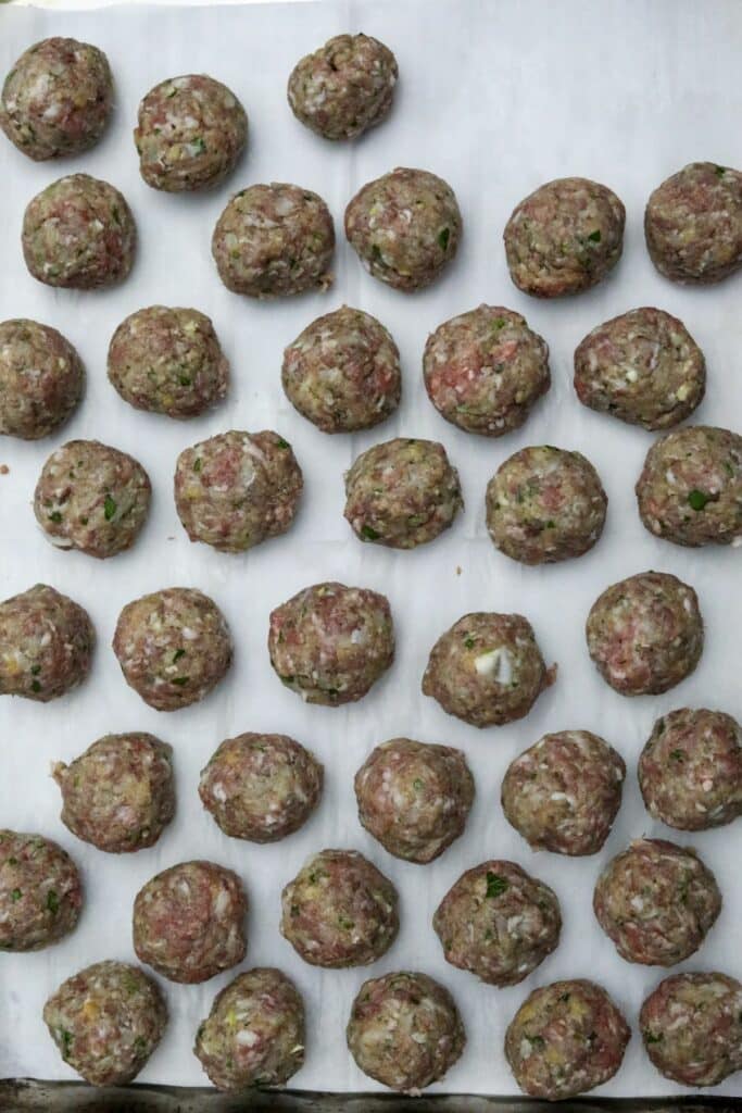 Raw meatballs on a parchment paper lined sheet pan