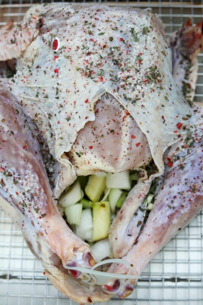 A turkey with the cavity filled with chopped vegetables and apples on a baking rack.