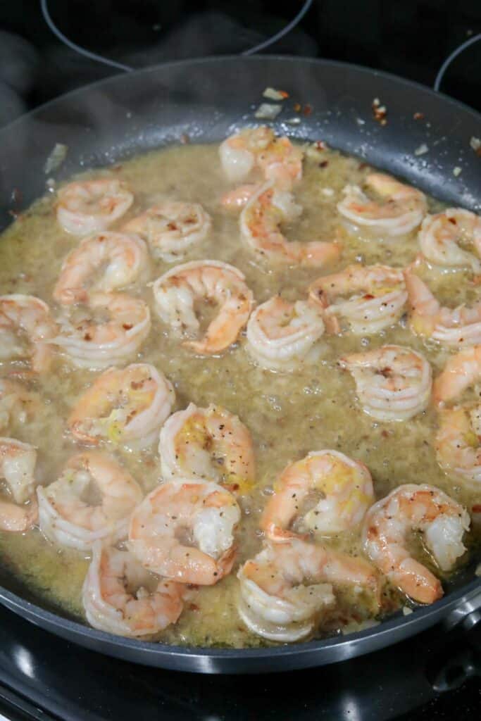 A pan with cooked shrimp and white wine sauce