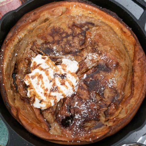 Whipped cream and syrup on a Dutch baby in a cast iron skillet
