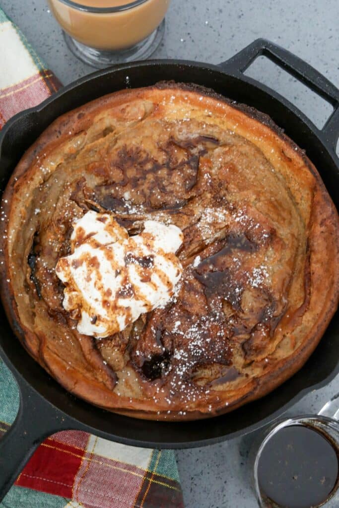 Whipped cream and syrup on a Dutch baby in a cast iron skillet