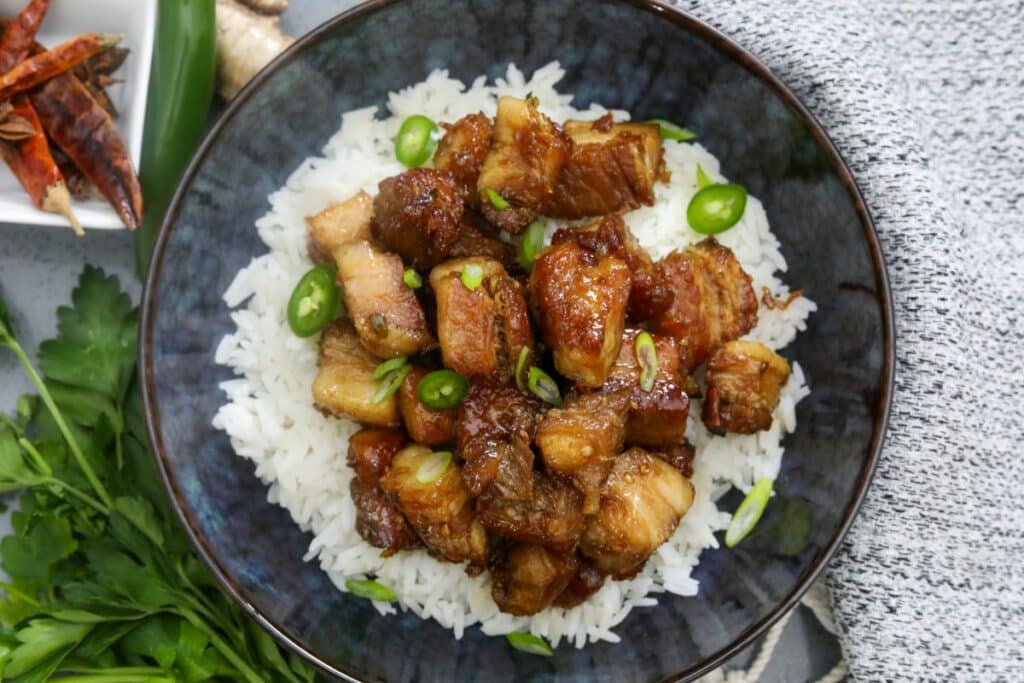 Soy glazed pork belly on a bed of rice in a blue bowl