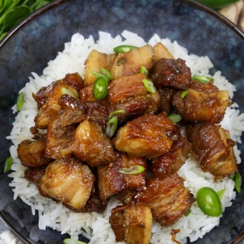A blue bowl with soy glazed pork belly on a bed of rice