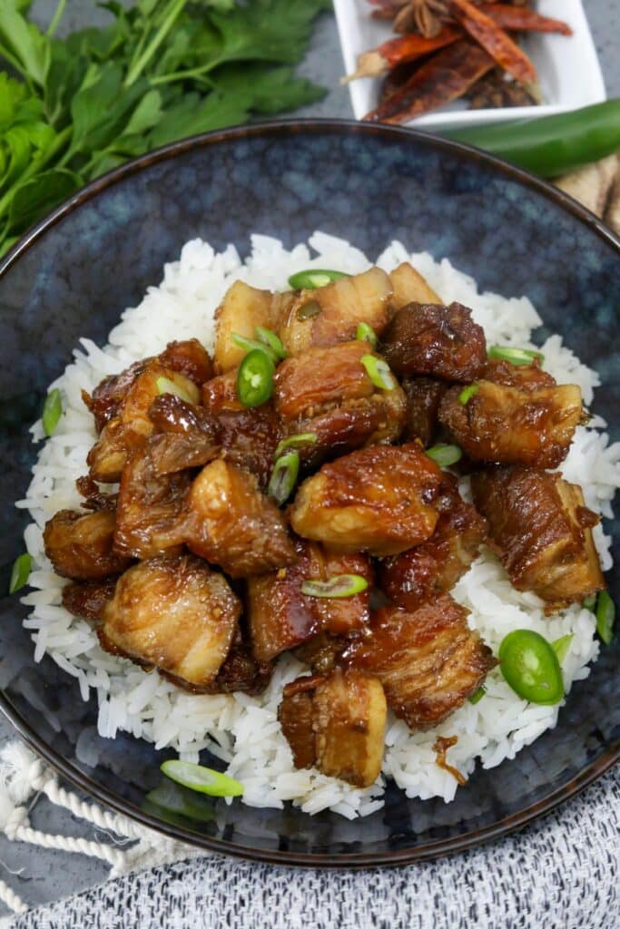 A blue bowl with soy glazed pork belly on a bed of rice